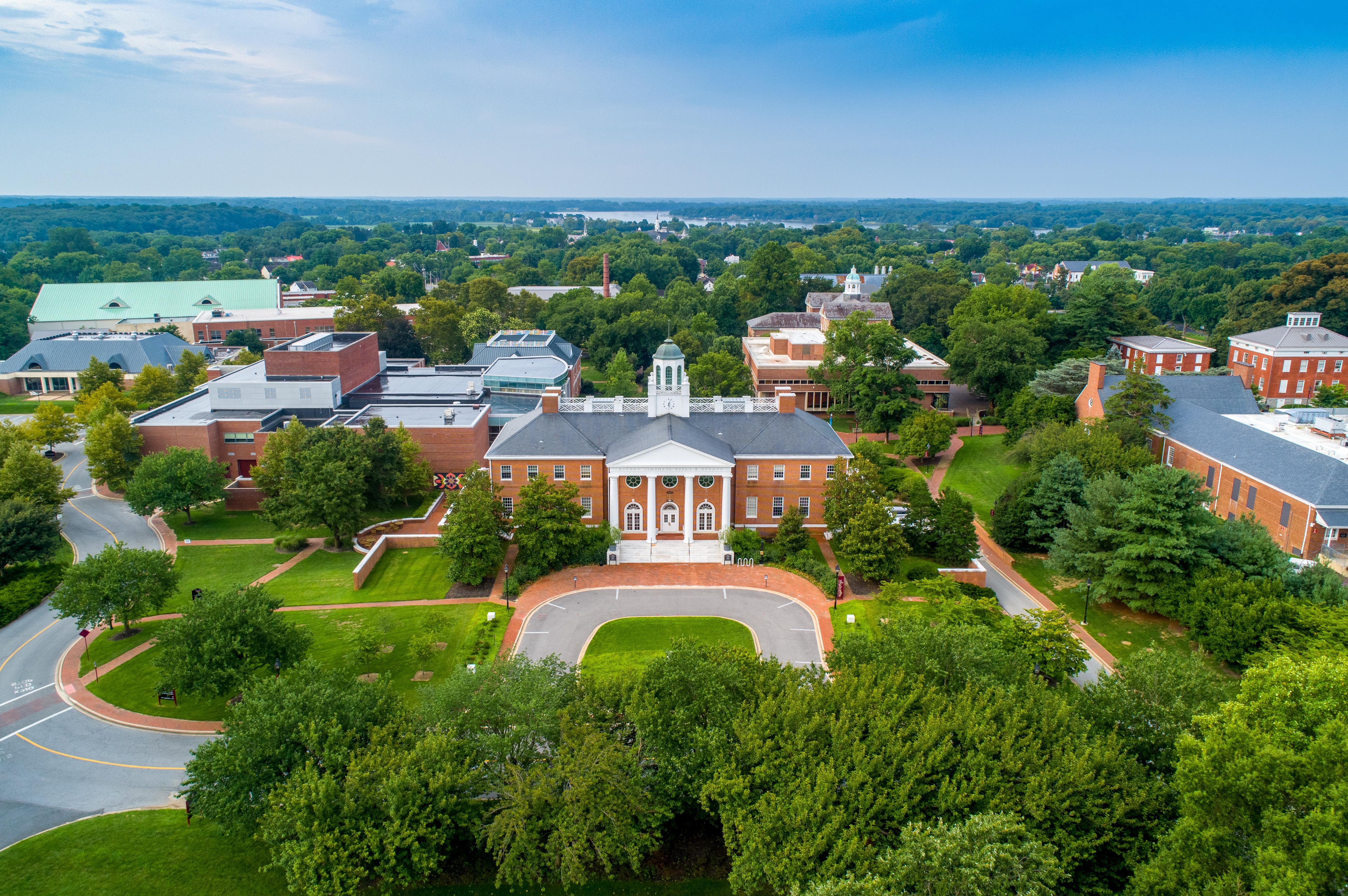 birds eye view of the casey academic center and campus during the spring. the sky is clear and the trees are lushious green